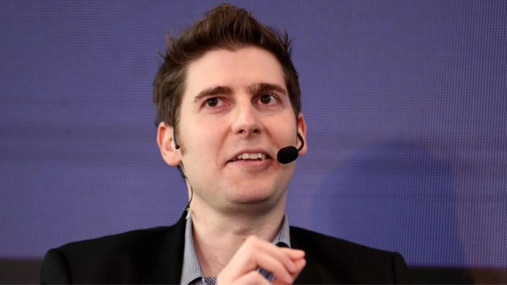 A professional headshot of Facebook co-founder Eduardo Saverin wearing a dark suit and a white shirt, looking directly at the camera with a confident smile.
