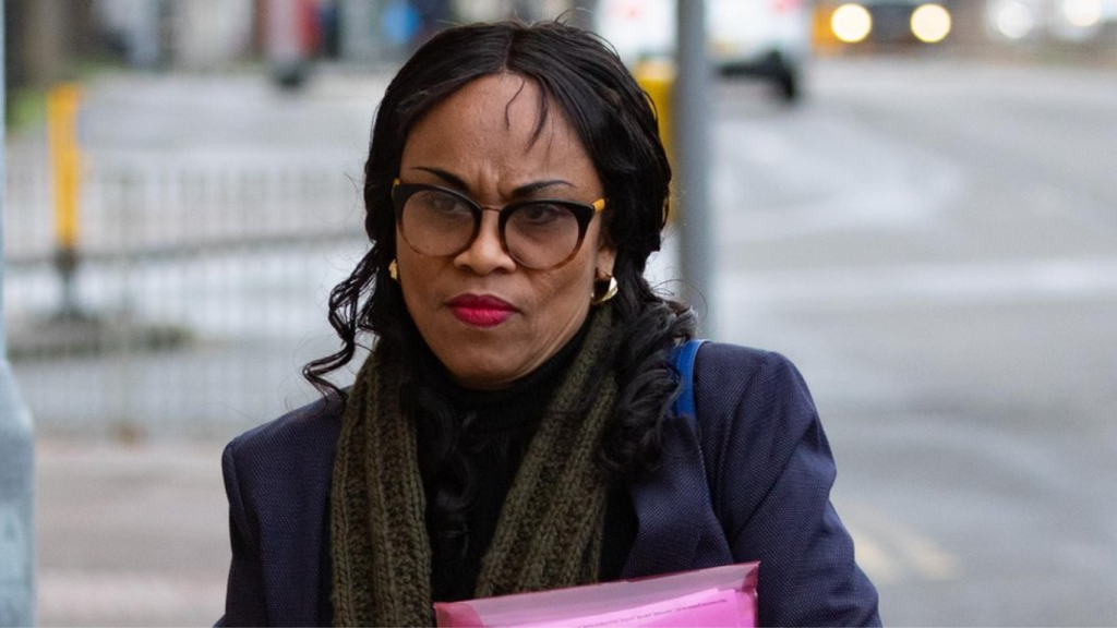 A professional portrait of Yinka Olatunji, mother of KSI and Deji, wearing a navy blazer and glasses.