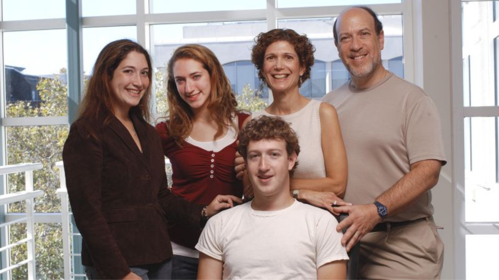 A group portrait of the Zuckerberg family, featuring Mark Zuckerberg sitting in the center surrounded by his parents, Edward and Karen Zuckerberg, and his sisters, Randi and Arielle, in a modern, well-lit room.