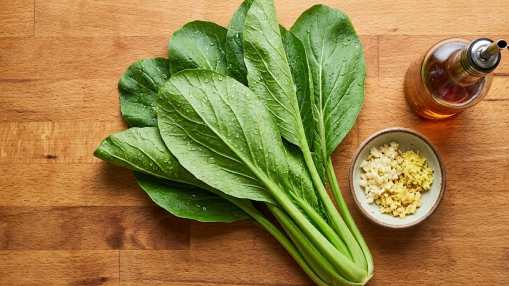 Fresh Yalla Choy leafy greens on a wooden kitchen counter with cooking ingredients.